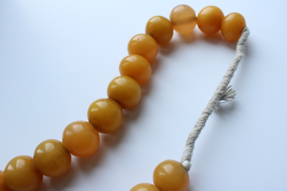 A continuous strand of smooth, round butterscotch yellow Bakelite beads strung on thread against a plain white background. View IV