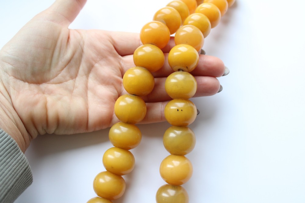 A continuous strand of smooth, round butterscotch yellow Bakelite beads strung on thread against a plain white background. View V