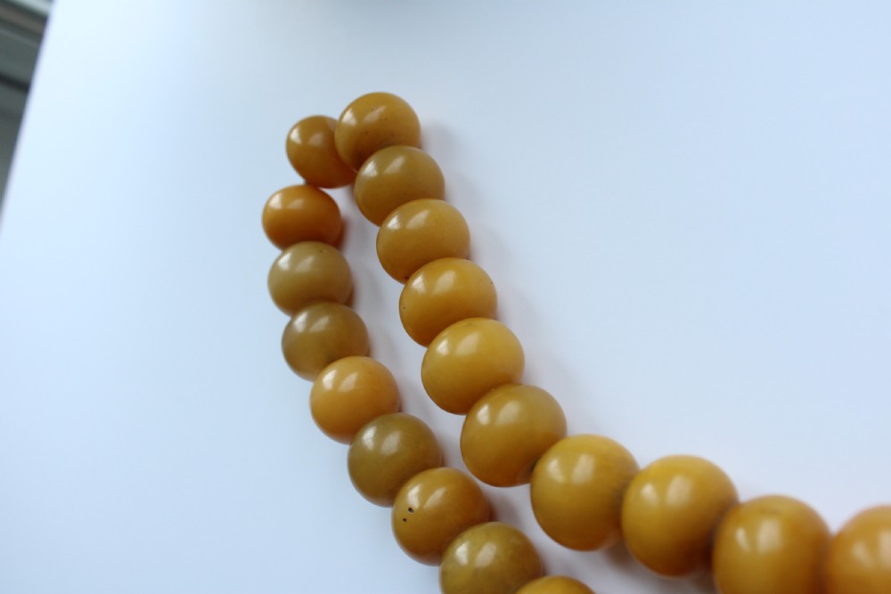 A continuous strand of smooth, round butterscotch yellow Bakelite beads strung on thread against a plain white background. View VI