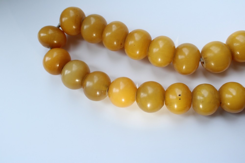 A continuous strand of smooth, round butterscotch yellow Bakelite beads strung on thread against a plain white background. View VII