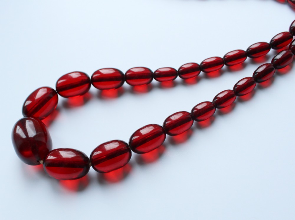 A continuous graduated strand of translucent cherry-red oval Bakelite beads displayed against a white background. View II