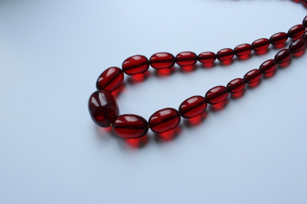 A continuous graduated strand of translucent cherry-red oval Bakelite beads displayed against a white background. View V