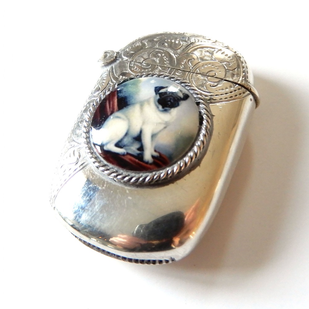 A sterling silver vesta case featuring an engraved top section, a rope-twist border, and a central enamel plaque depicting a sitting pug dog.