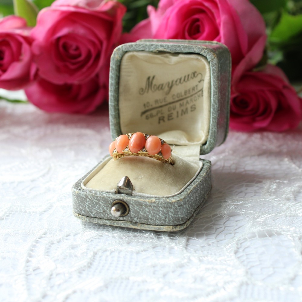 An antique 18ct yellow gold ring featuring five oval coral cabochons set in a boat-shaped gallery with small diamond accents.