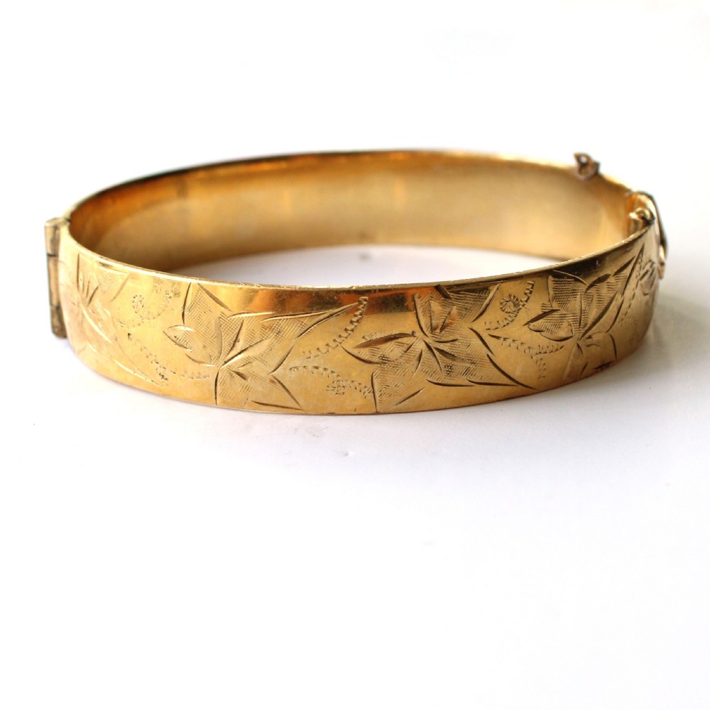 A vintage gold-toned hinged bangle bracelet featuring etched floral and leaf motifs around the outer circumference. View IV