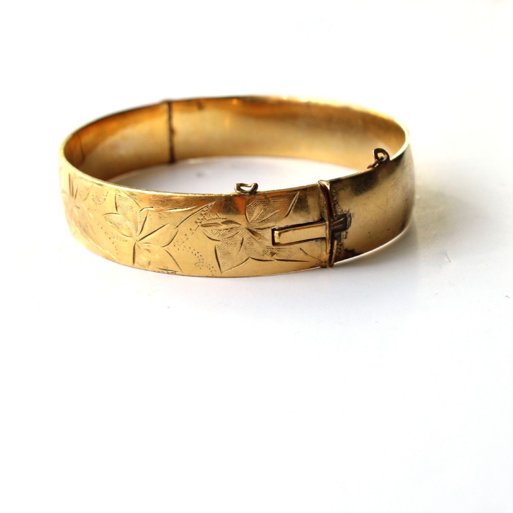 A vintage gold-toned hinged bangle bracelet featuring etched floral and leaf motifs around the outer circumference. View V
