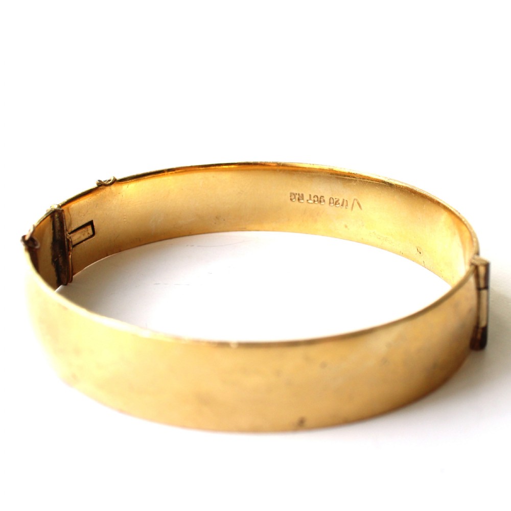A vintage gold-toned hinged bangle bracelet featuring etched floral and leaf motifs around the outer circumference. View VI