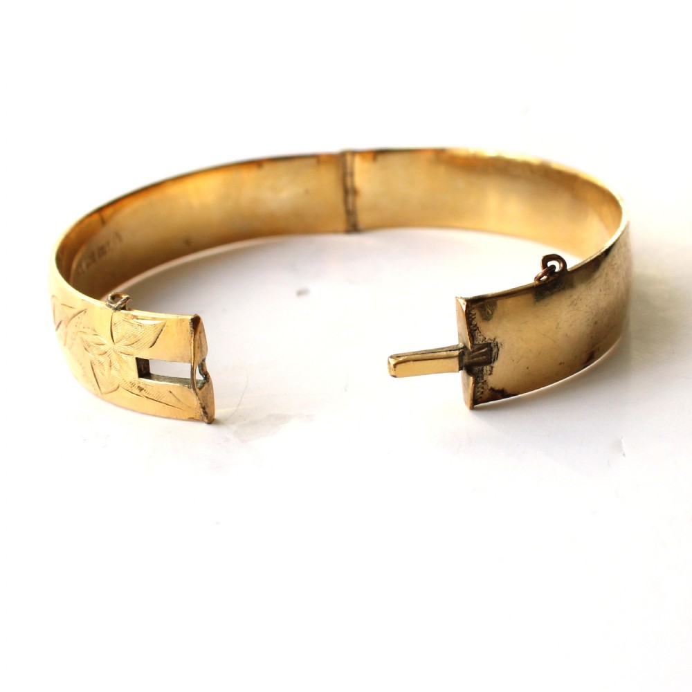 A vintage gold-toned hinged bangle bracelet featuring etched floral and leaf motifs around the outer circumference. View VII