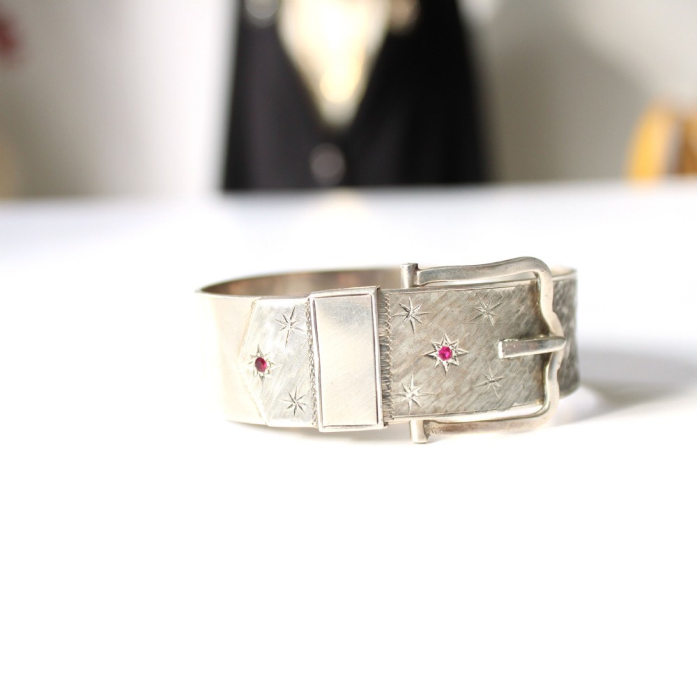 A wide sterling silver hinged buckle bangle featuring engraved starburst patterns set with round red rubies. View III