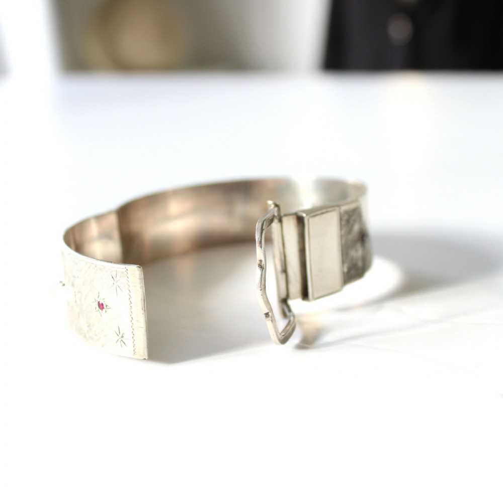 A wide sterling silver hinged buckle bangle featuring engraved starburst patterns set with round red rubies. View VI