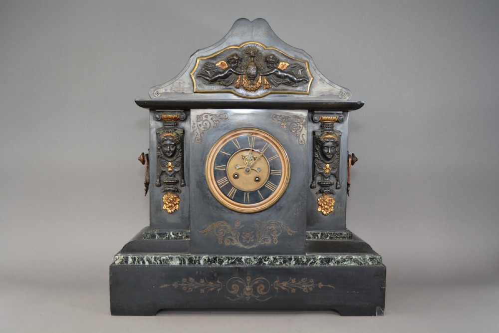 A Victorian black slate and green marble mantel clock featuring bronze mounts, gilt etched scrollwork, and classical cherub reliefs.