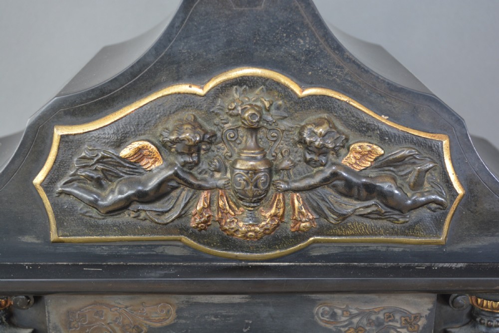 A Victorian black slate and green marble mantel clock featuring bronze mounts, gilt etched scrollwork, and classical cherub reliefs. View VI