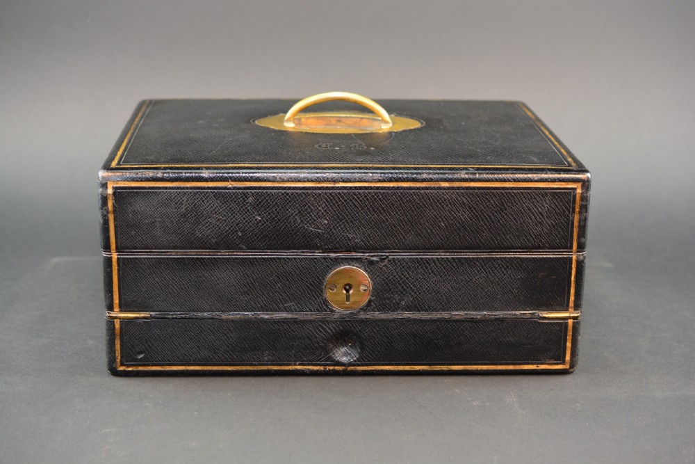 A rectangular black leather Victorian writing box featuring gilt-tooled border lines, a top brass carrying handle, and a central brass keyhole escutcheon.