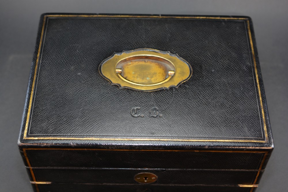 A rectangular black leather Victorian writing box featuring gilt-tooled border lines, a top brass carrying handle, and a central brass keyhole escutcheon. View II