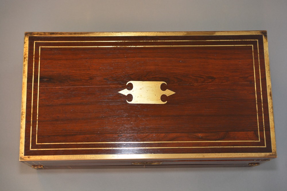 Top view of a rectangular dark rosewood writing slope decorated with brass border stringing and a central brass cartouche.
