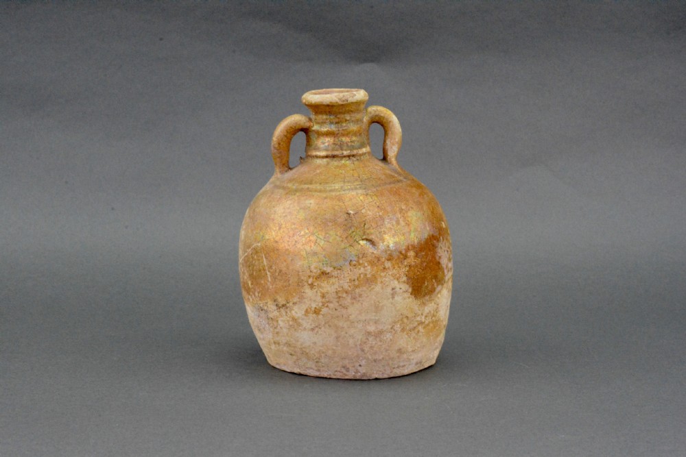 A small late Roman ceramic flask with twin looped handles, a rounded earthenware body, and a weathered yellowish-brown glaze.