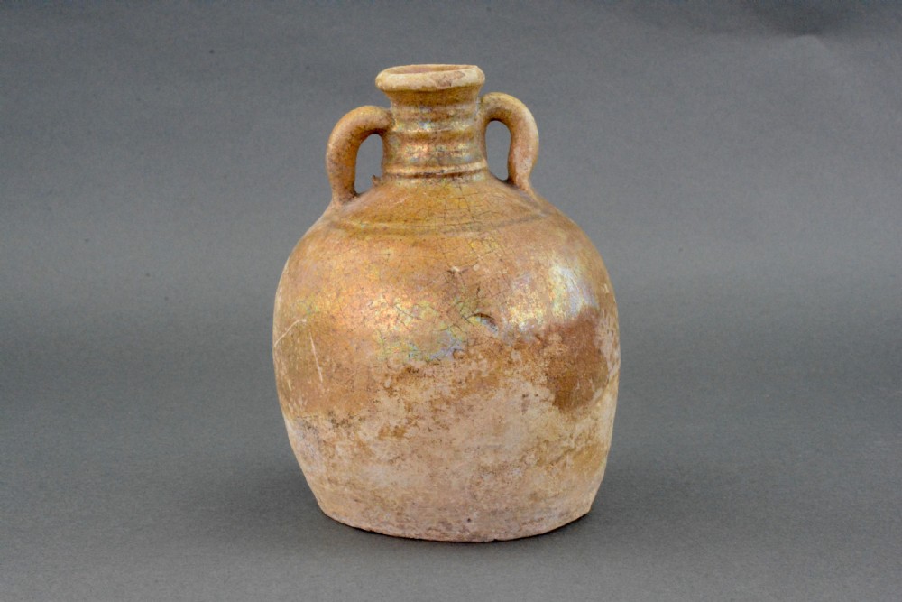 A small late Roman ceramic flask with twin looped handles, a rounded earthenware body, and a weathered yellowish-brown glaze. View II
