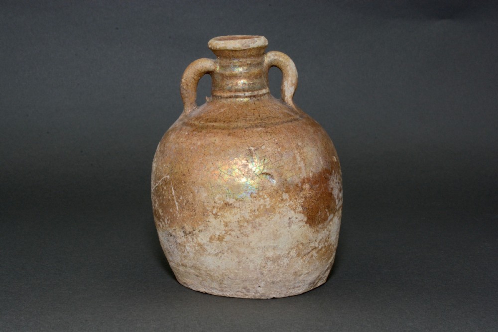 A small late Roman ceramic flask with twin looped handles, a rounded earthenware body, and a weathered yellowish-brown glaze. View III