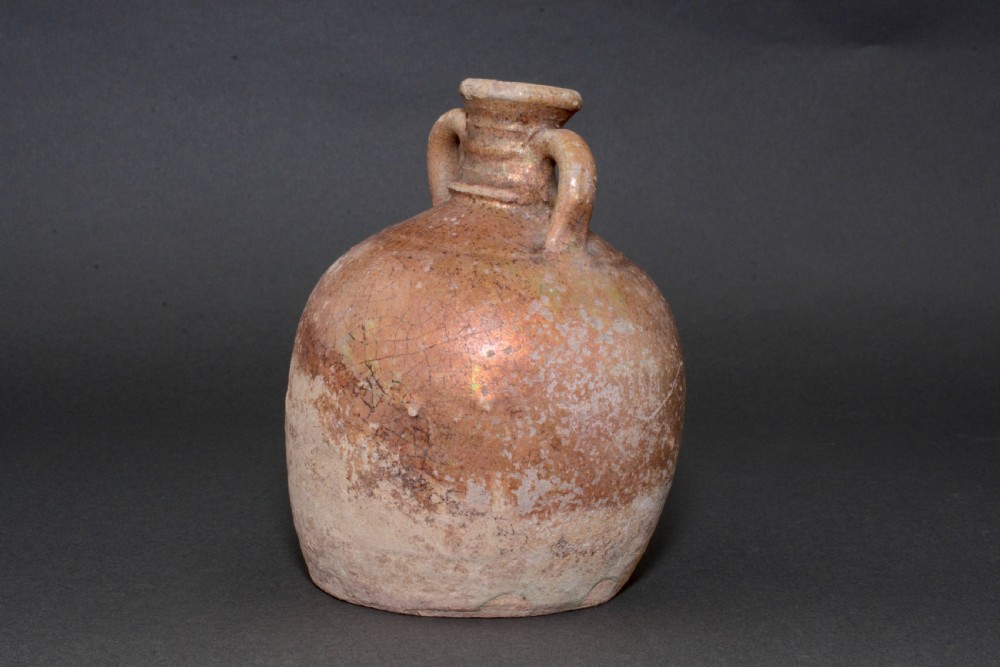 A small late Roman ceramic flask with twin looped handles, a rounded earthenware body, and a weathered yellowish-brown glaze. View IV