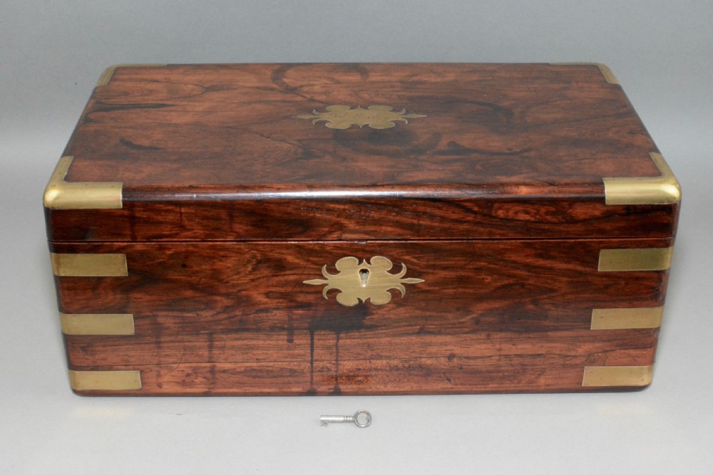 A rectangular dark wood writing slope box with flush brass corner brackets, a brass keyhole escutcheon, and an inlaid top plaque.