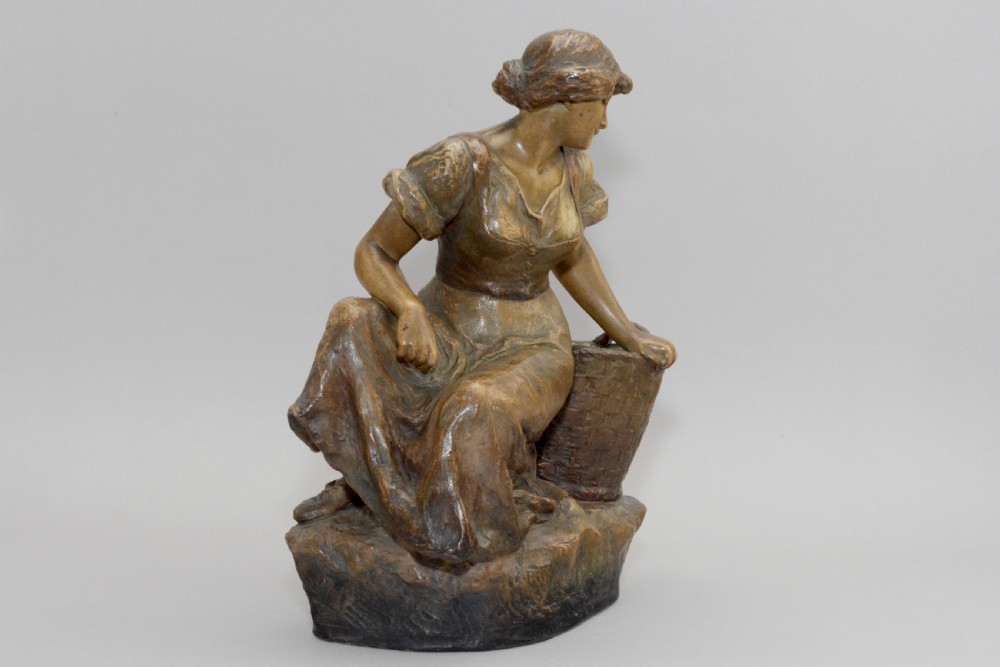 An Art Nouveau terracotta sculpture depicting a seated country maiden in draped clothing beside a woven basket. View II