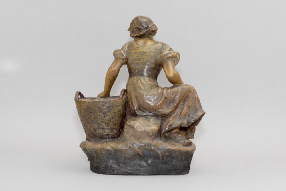 An Art Nouveau terracotta sculpture depicting a seated country maiden in draped clothing beside a woven basket. View III