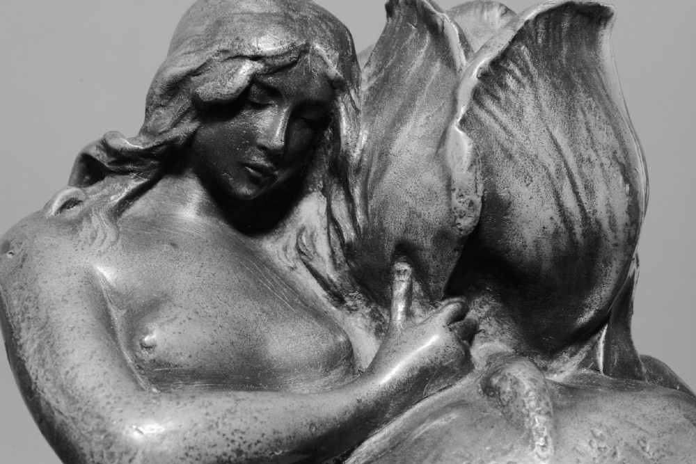 A pair of Art Nouveau pewter candlesticks modelled as draped female figures embracing large flower blossoms on lily pad bases. View VII
