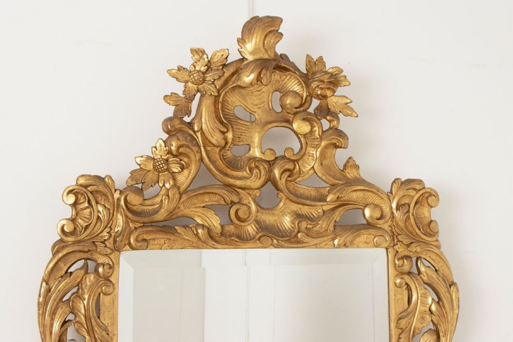 A 19th-century Italian giltwood wall mirror featuring an ornate carved floral cresting and rectangular bevelled glass. View II