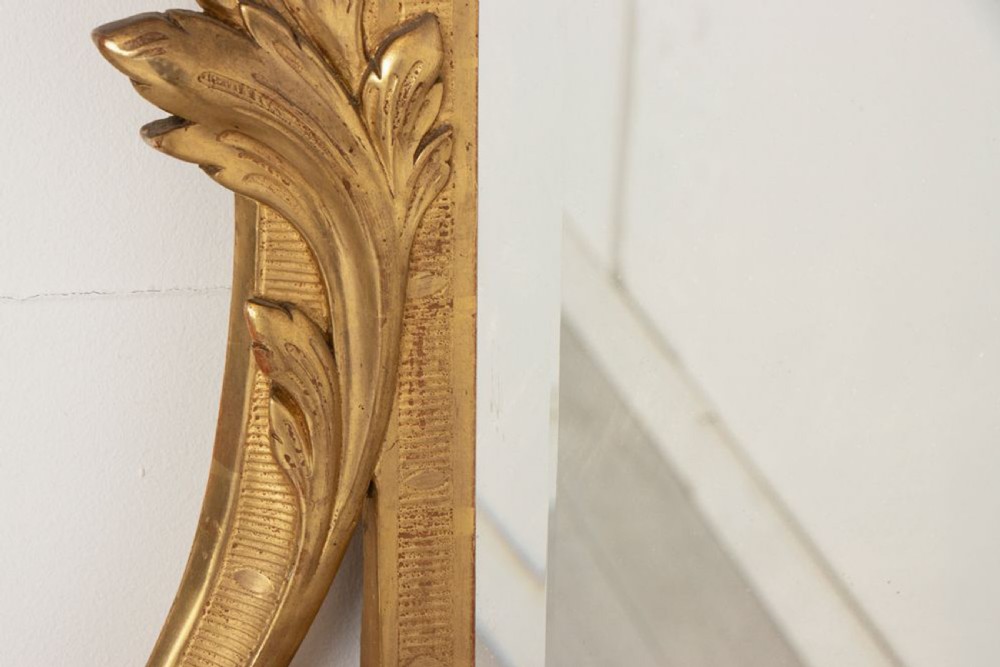 A 19th-century Italian giltwood wall mirror featuring an ornate carved floral cresting and rectangular bevelled glass. View IV