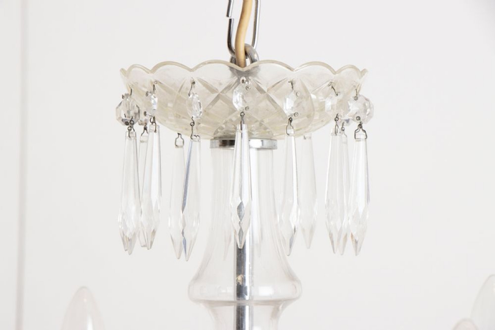 A 1920s clear glass chandelier featuring curved swan-style arms, candle-shaped light sockets, hanging crystal droplets, and a silver ceiling chain. View IV