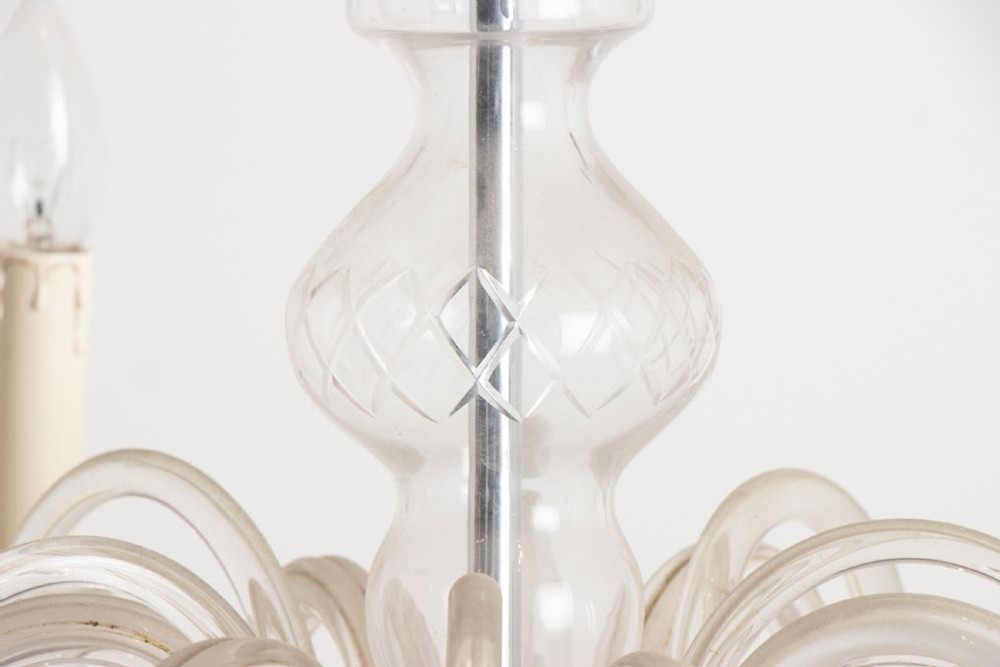 A 1920s clear glass chandelier featuring curved swan-style arms, candle-shaped light sockets, hanging crystal droplets, and a silver ceiling chain. View V