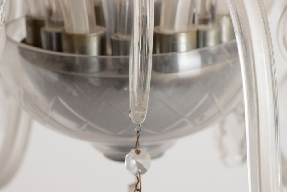 A 1920s clear glass chandelier featuring curved swan-style arms, candle-shaped light sockets, hanging crystal droplets, and a silver ceiling chain. View VII