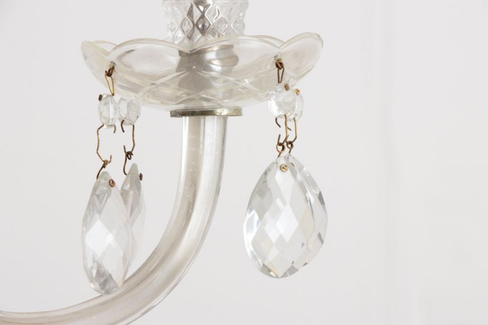 A 1920s clear glass chandelier featuring curved swan-style arms, candle-shaped light sockets, hanging crystal droplets, and a silver ceiling chain. View IX