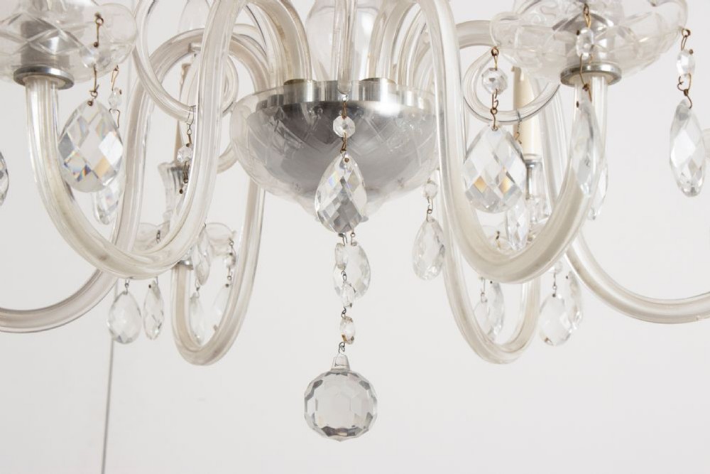 A 1920s clear glass chandelier featuring curved swan-style arms, candle-shaped light sockets, hanging crystal droplets, and a silver ceiling chain. View XI