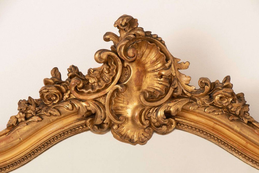 An upright rectangular French giltwood wall mirror featuring a crested top with acanthus leaf ornamentation and subtle red bole showing beneath the gold leaf finish. View II