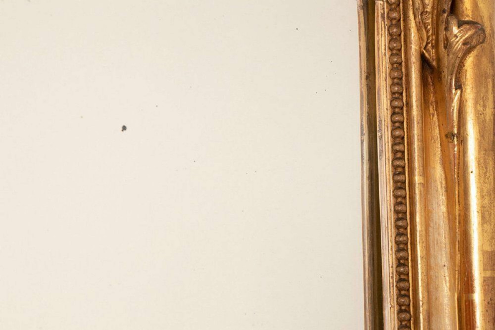 An upright rectangular French giltwood wall mirror featuring a crested top with acanthus leaf ornamentation and subtle red bole showing beneath the gold leaf finish. View IX