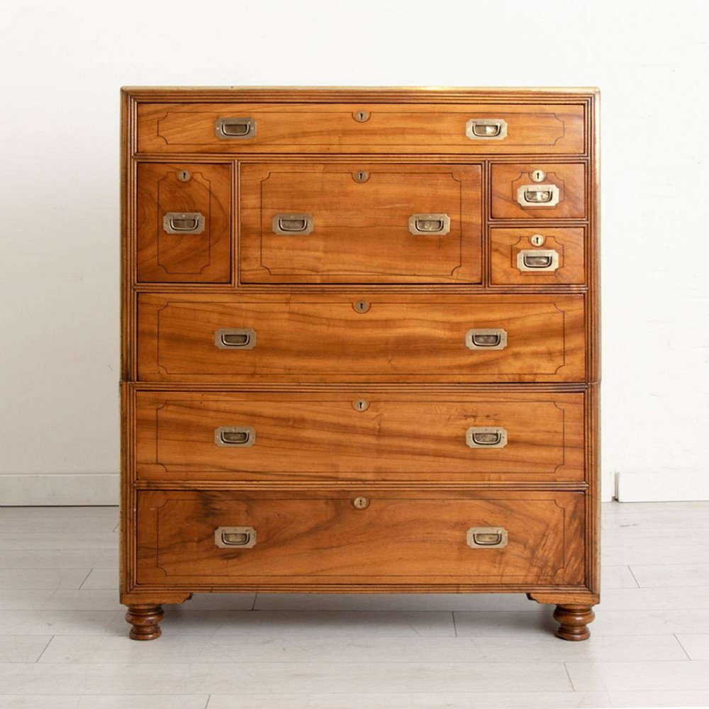 An antique 19th-century camphorwood military campaign secretaire chest featuring flush brass handles, geometric drawer borders, and turned feet.