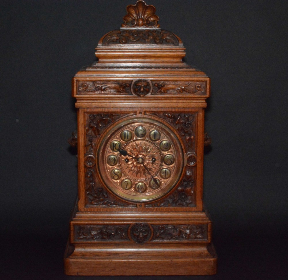 A hand-carved oak mantel clock featuring a central copper dial with raised numerals, flanked by intricate foliate carvings and topped with a shell finial.