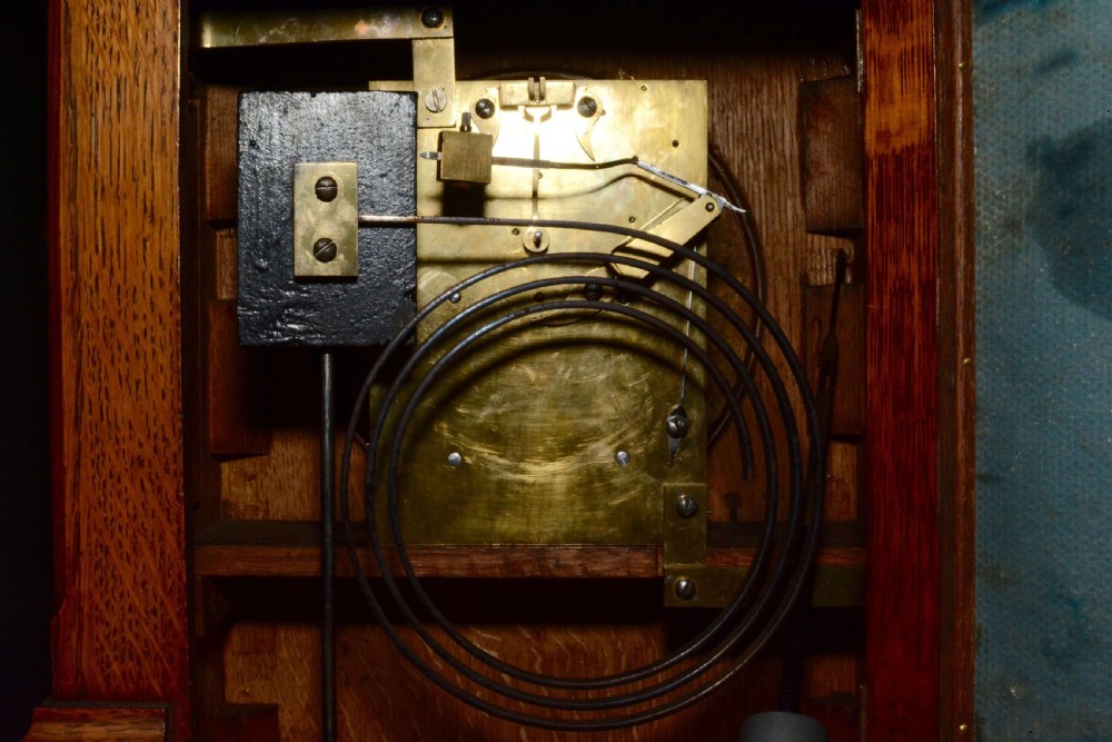 A hand-carved oak mantel clock featuring a central copper dial with raised numerals, flanked by intricate foliate carvings and topped with a shell finial. View VI