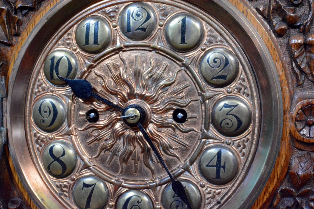 A hand-carved oak mantel clock featuring a central copper dial with raised numerals, flanked by intricate foliate carvings and topped with a shell finial. View VIII