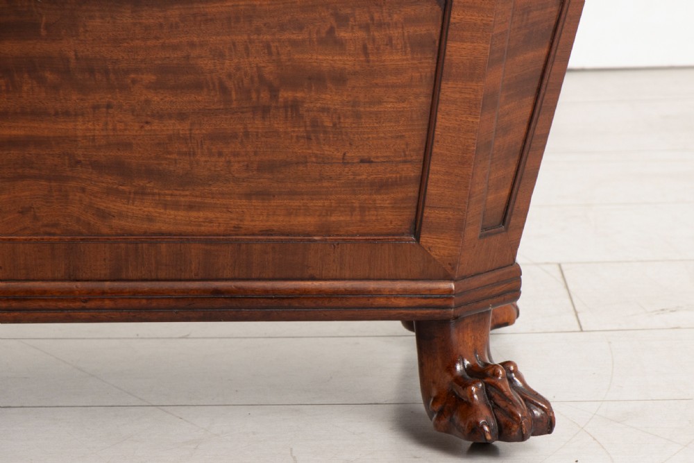 A Georgian mahogany sarcophagus-shaped cellarette featuring a stepped lid, brass escutcheon, flame veneer panels, and carved paw feet. View IV