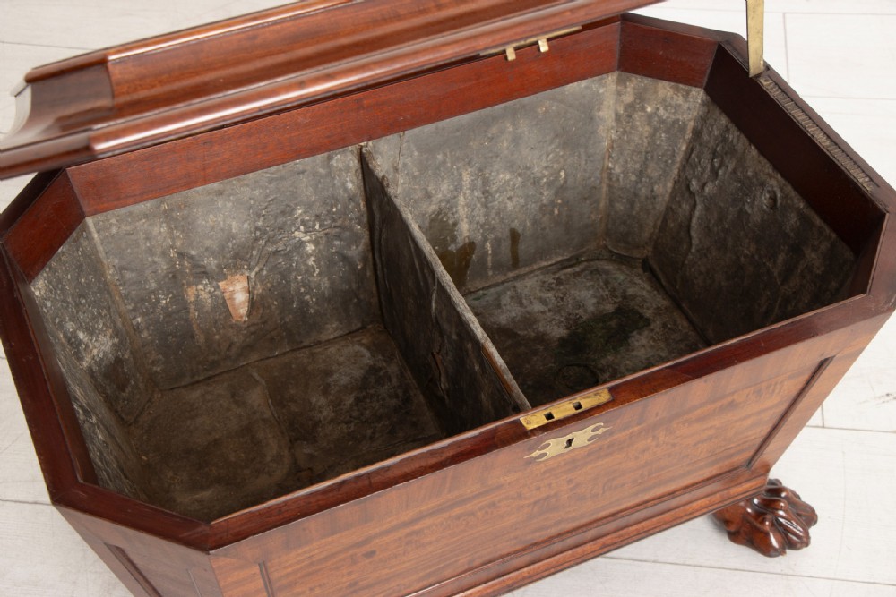 A Georgian mahogany sarcophagus-shaped cellarette featuring a stepped lid, brass escutcheon, flame veneer panels, and carved paw feet. View IX
