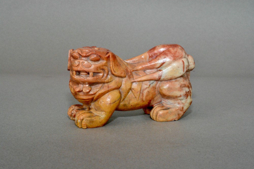 A hand-carved soapstone sculpture depicting a Chinese guardian foo dog in tones of terracotta brown, ochre, and cream.
