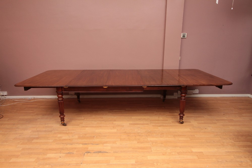 A extended Cuban mahogany dining table featuring additional insert leaves, a polished rectangular top, and four reeded turned legs on brass castors.