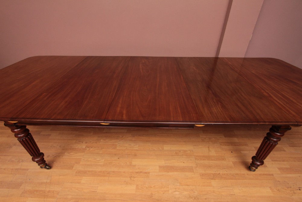 A extended Cuban mahogany dining table featuring additional insert leaves, a polished rectangular top, and four reeded turned legs on brass castors. View II