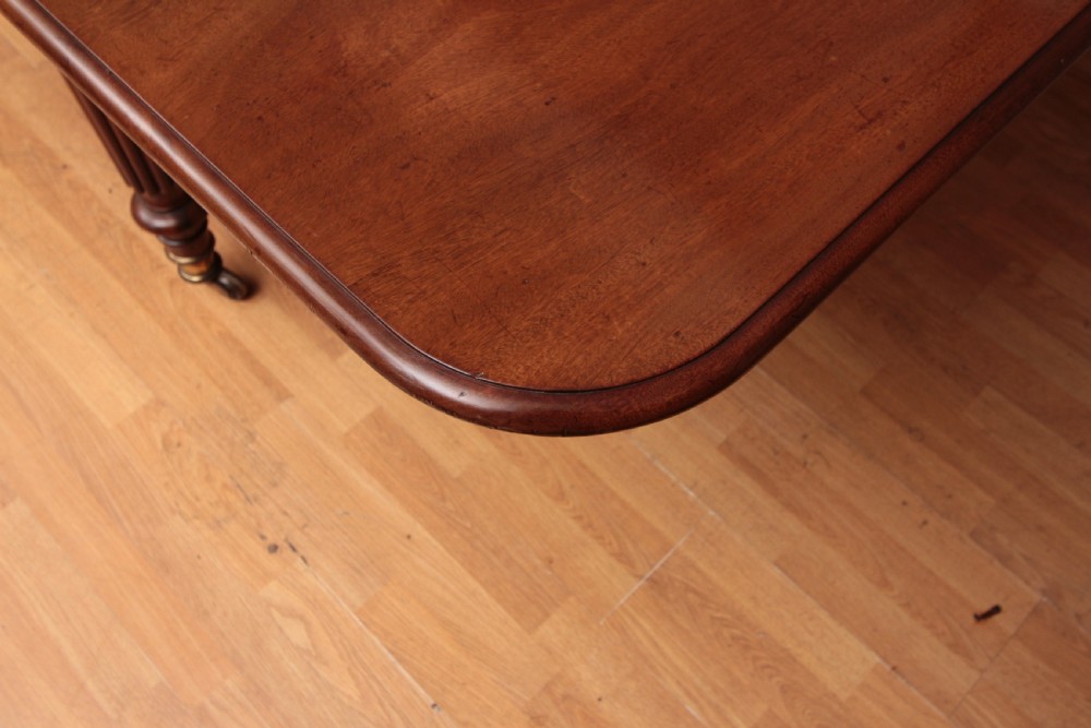 A extended Cuban mahogany dining table featuring additional insert leaves, a polished rectangular top, and four reeded turned legs on brass castors. View IV