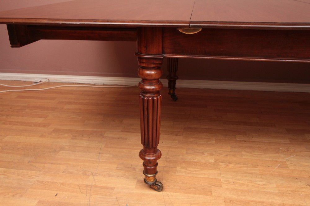 A extended Cuban mahogany dining table featuring additional insert leaves, a polished rectangular top, and four reeded turned legs on brass castors. View V