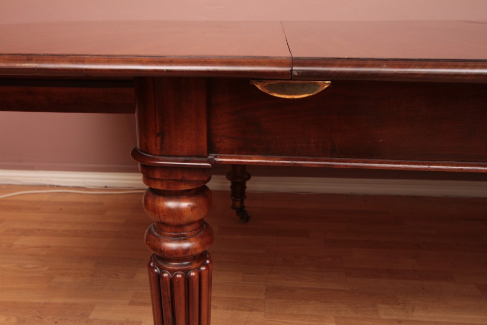 A extended Cuban mahogany dining table featuring additional insert leaves, a polished rectangular top, and four reeded turned legs on brass castors. View VII
