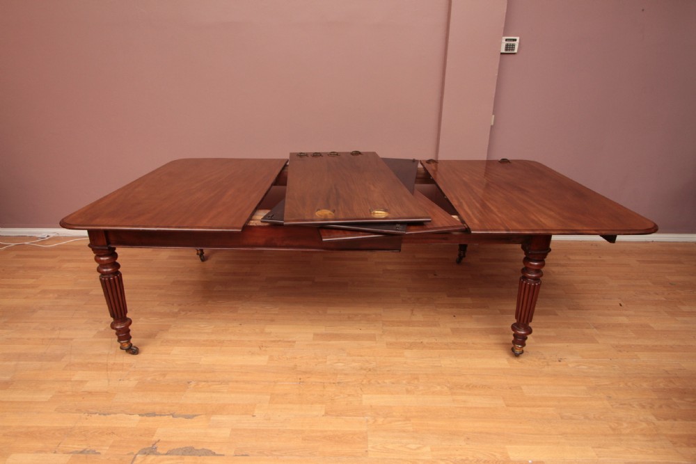 A extended Cuban mahogany dining table featuring additional insert leaves, a polished rectangular top, and four reeded turned legs on brass castors. View VIII