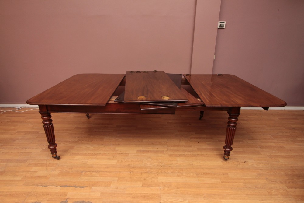 A extended Cuban mahogany dining table featuring additional insert leaves, a polished rectangular top, and four reeded turned legs on brass castors. View IX